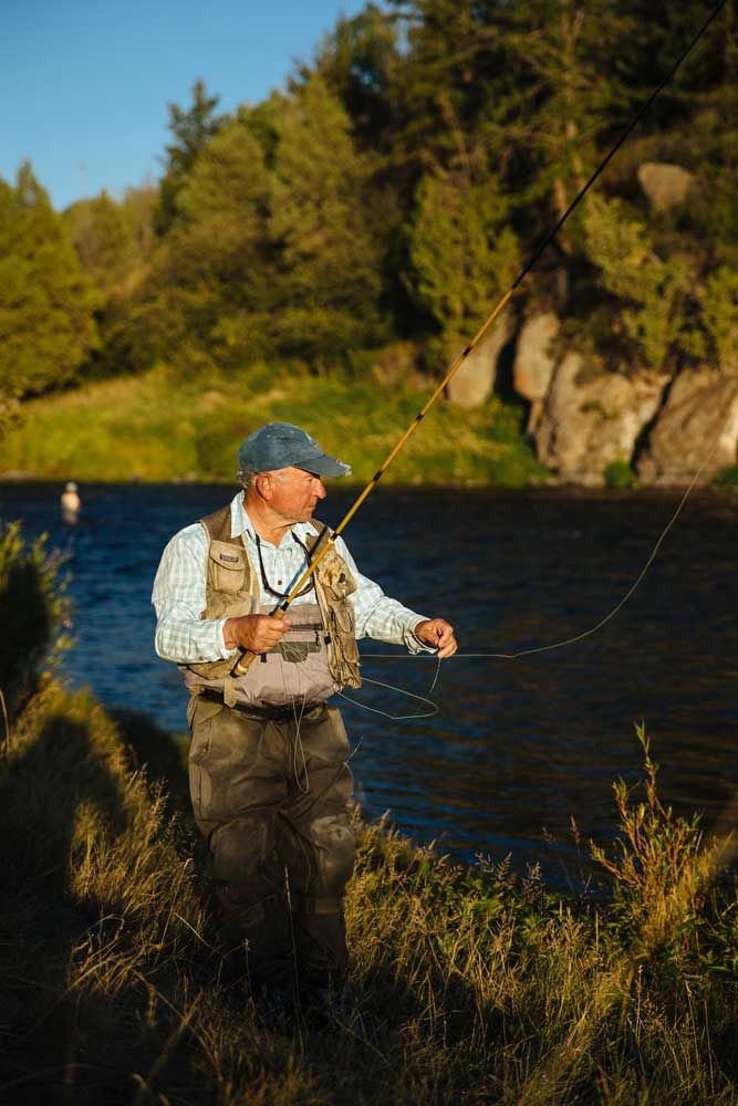 a man standing on the side of a river while holding onto a fishing line and hook