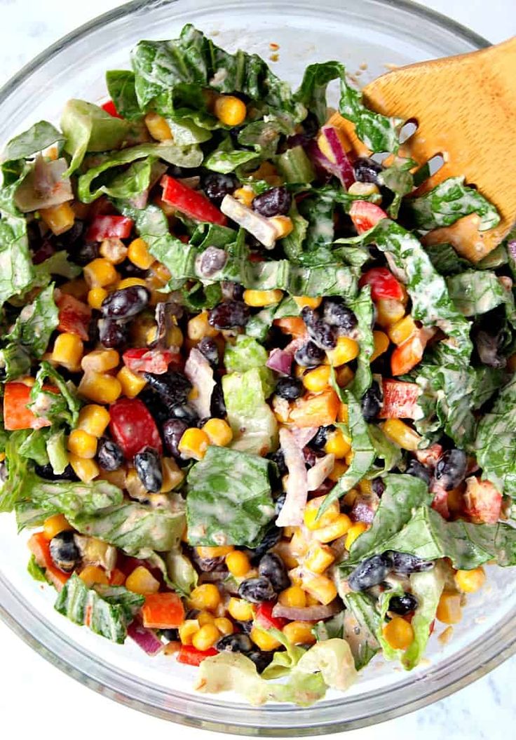 a salad in a glass bowl with a wooden spoon on the side, ready to be eaten