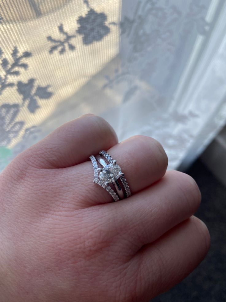 a person's hand with a diamond ring on top of their finger, in front of a window