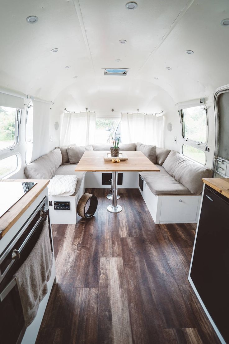 the interior of an rv with wood flooring and white walls, windows, and couches