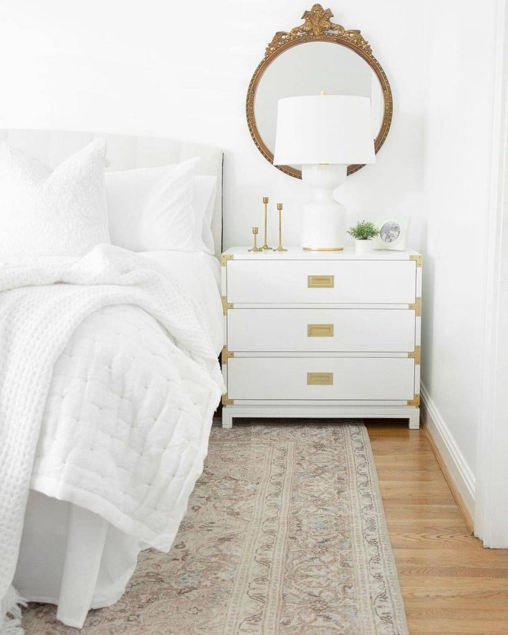 a bedroom with white bedding, gold accents and a large mirror on the wall