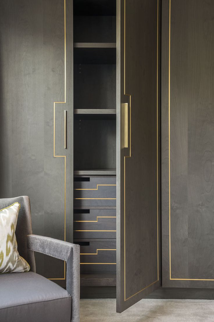 an armoire with gold trim and drawers in a room that has grey walls, carpeted flooring and a gray chair next to it