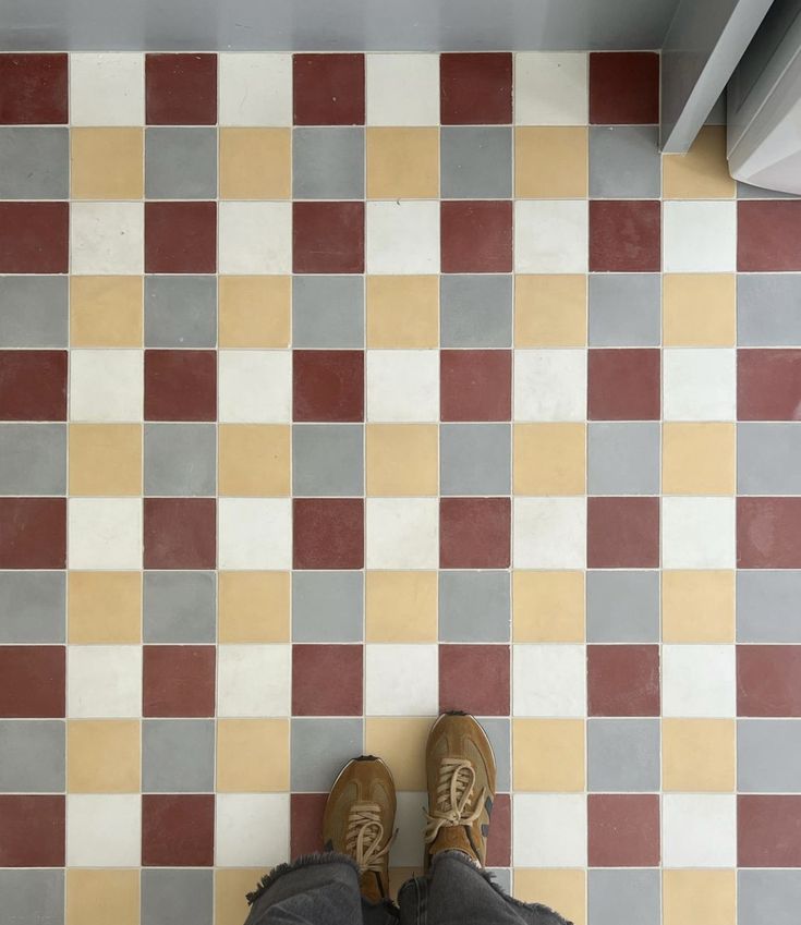 a person's feet standing in front of a checkered floor with red, yellow and grey tiles