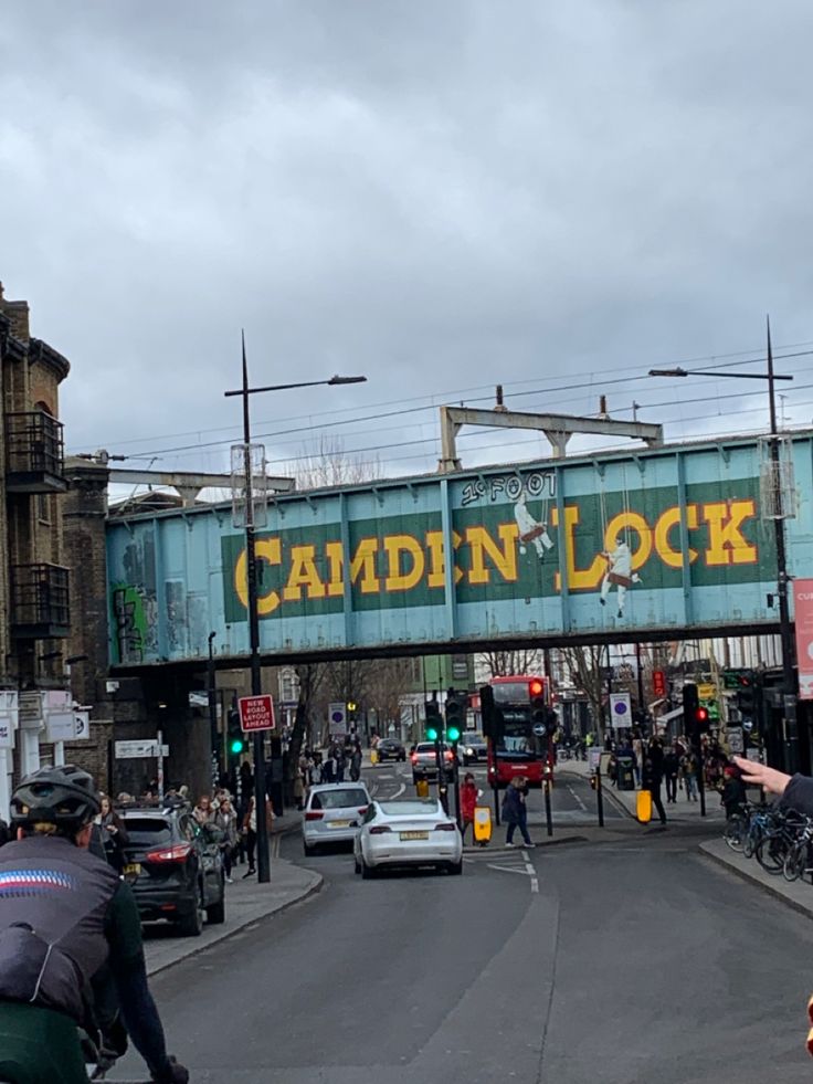 a group of people riding bikes down a street next to a blue bridge with the words camden lock on it