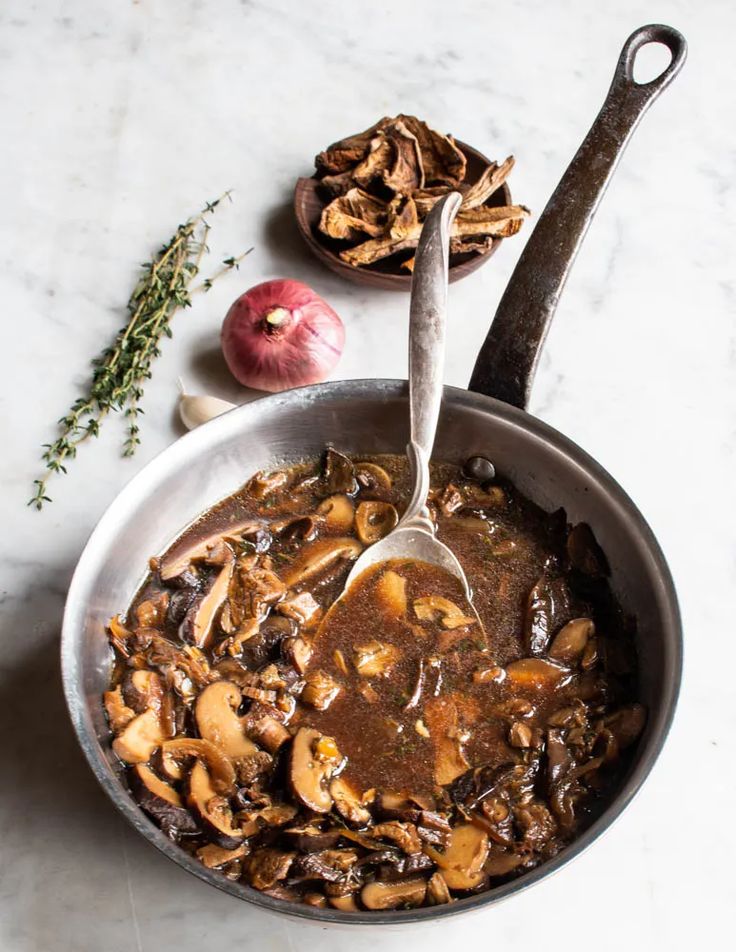 a pan filled with mushroom stew next to an apple