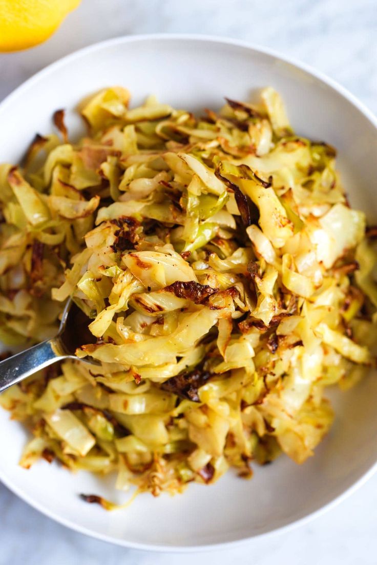 a white bowl filled with chopped up cabbage next to an orange wedged in half