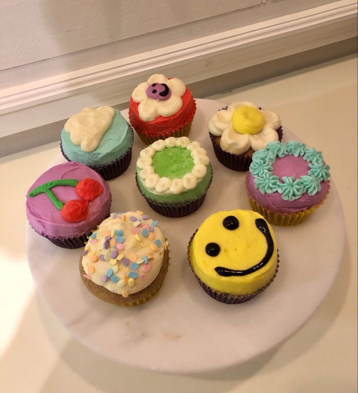 there are many cupcakes on the plate with smiley face and flower decorations around them