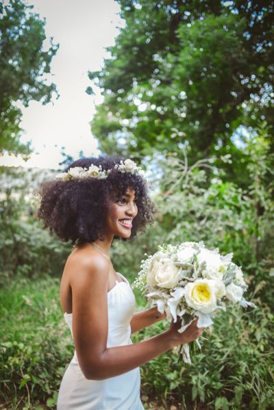 a woman in a white dress holding a bouquet of flowers and smiling at the camera