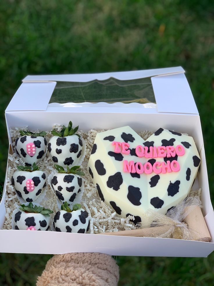 someone is holding up a box with some chocolates in it and a heart shaped cake