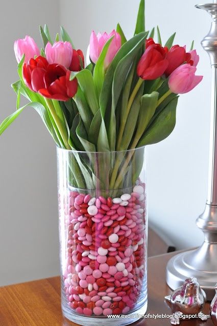 a vase filled with lots of pink and red candy covered flowers on top of a wooden table