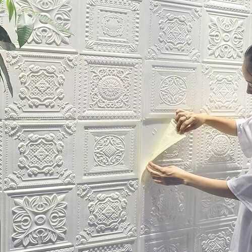 a woman is working on a wall with white paint and decorative plaster tiles in front of her