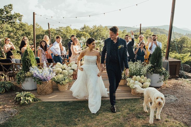 a bride and groom walking down the aisle with their dog in front of an outdoor ceremony