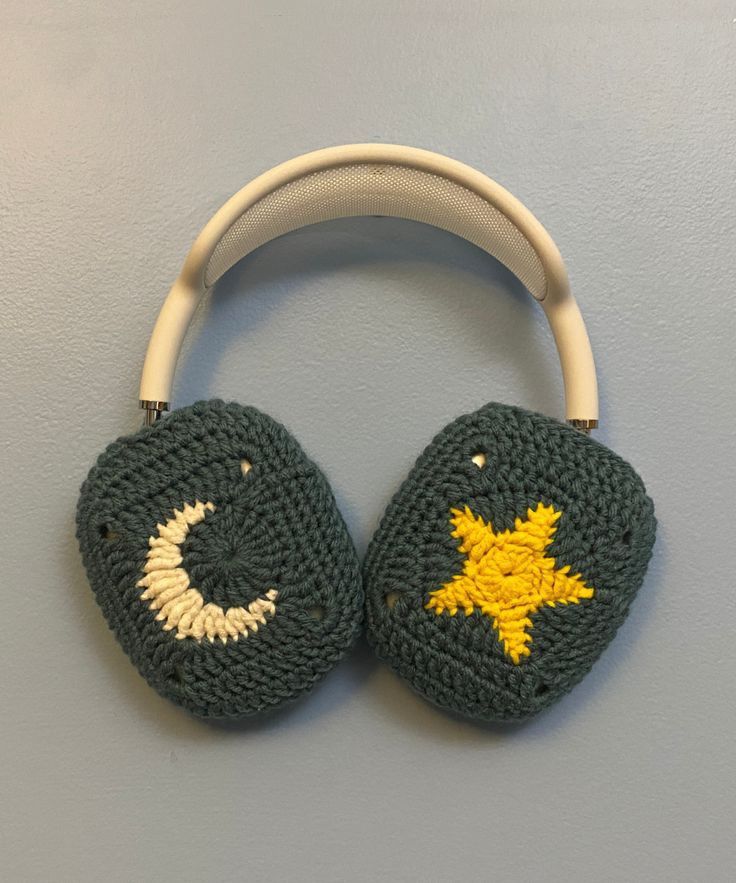 two crocheted headphones hanging from a hook on a gray wall with a yellow star and crescent design