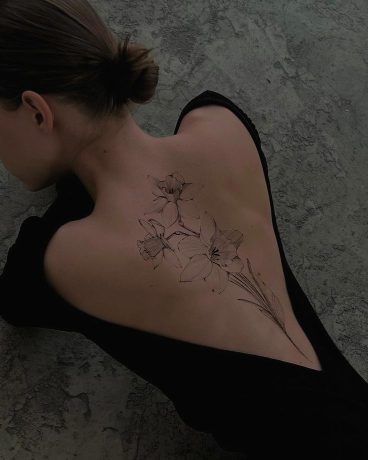 a woman with a flower tattoo on her back and shoulder is looking down at the ground