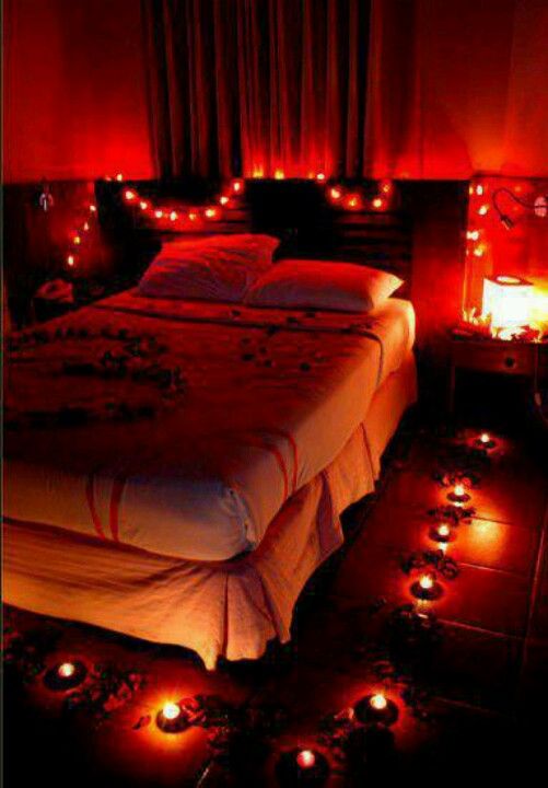 a bed with lots of candles on the floor next to it and a red light in the bedroom