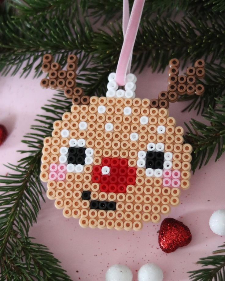 a cross stitch ornament hanging from a christmas tree with ornaments around it on a pink surface