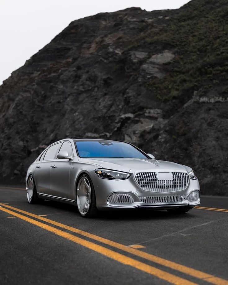 a silver mercedes s - class driving down the road in front of a large mountain