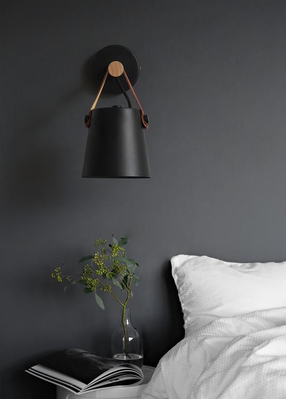 a black lamp hanging over a bed next to a vase with a plant in it