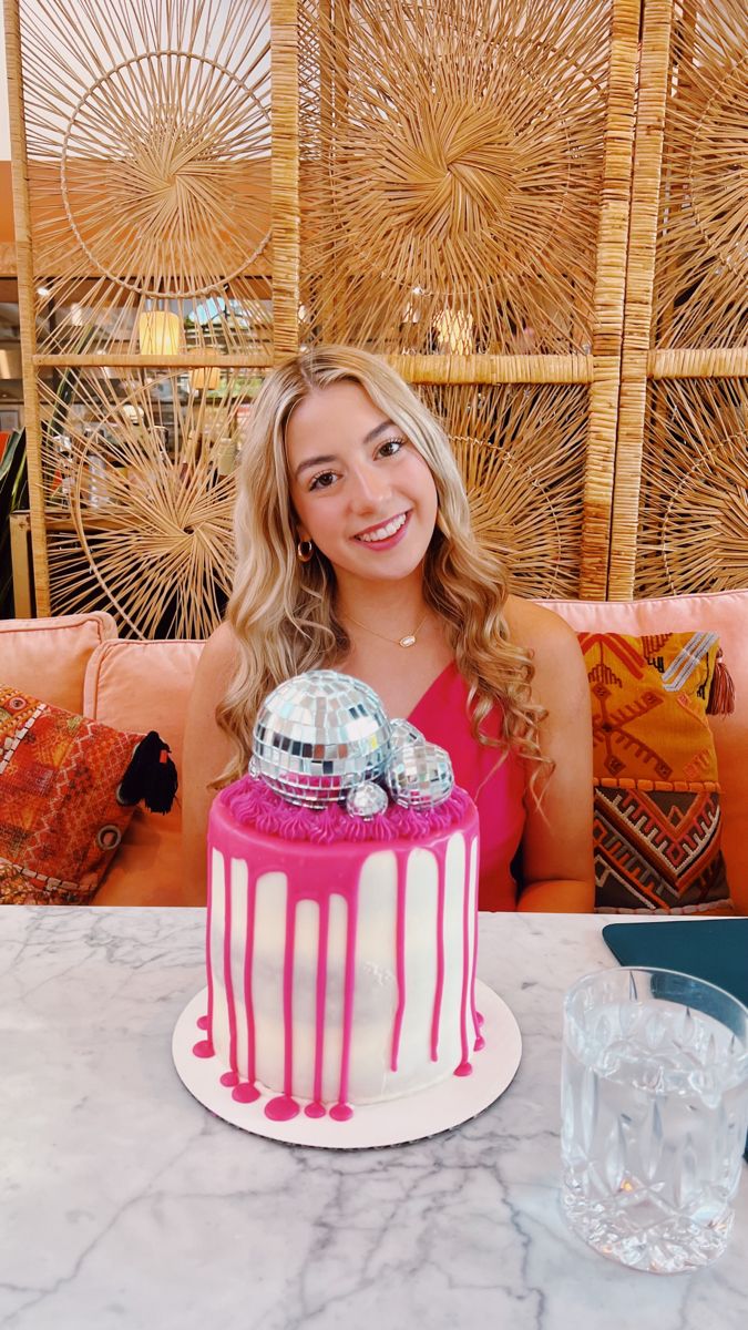 a woman sitting at a table with a pink and white cake in front of her