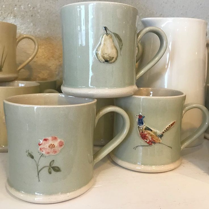 several coffee mugs with birds and flowers on them sitting on a counter next to other cups