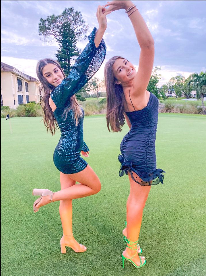 two beautiful young women standing next to each other on top of a lush green field