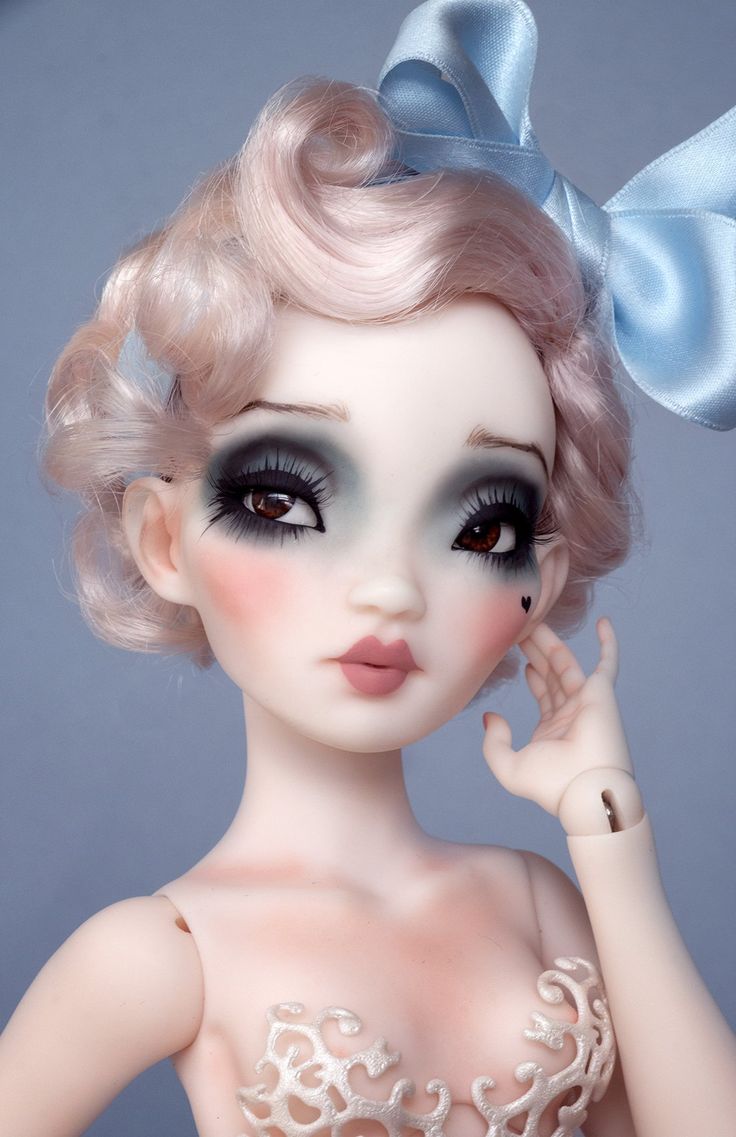 a close up of a doll with blonde hair and black eyeliners wearing a blue bow