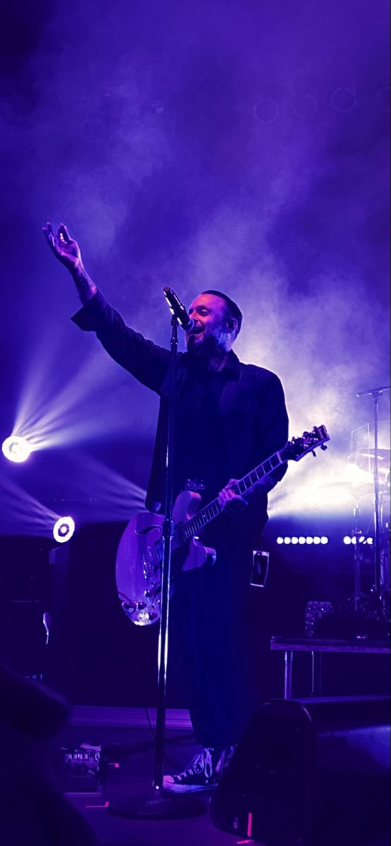 a man standing in front of a microphone on stage with his hand up to the sky