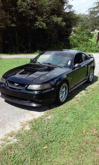 a black car parked on the side of a road next to grass and trees in the background