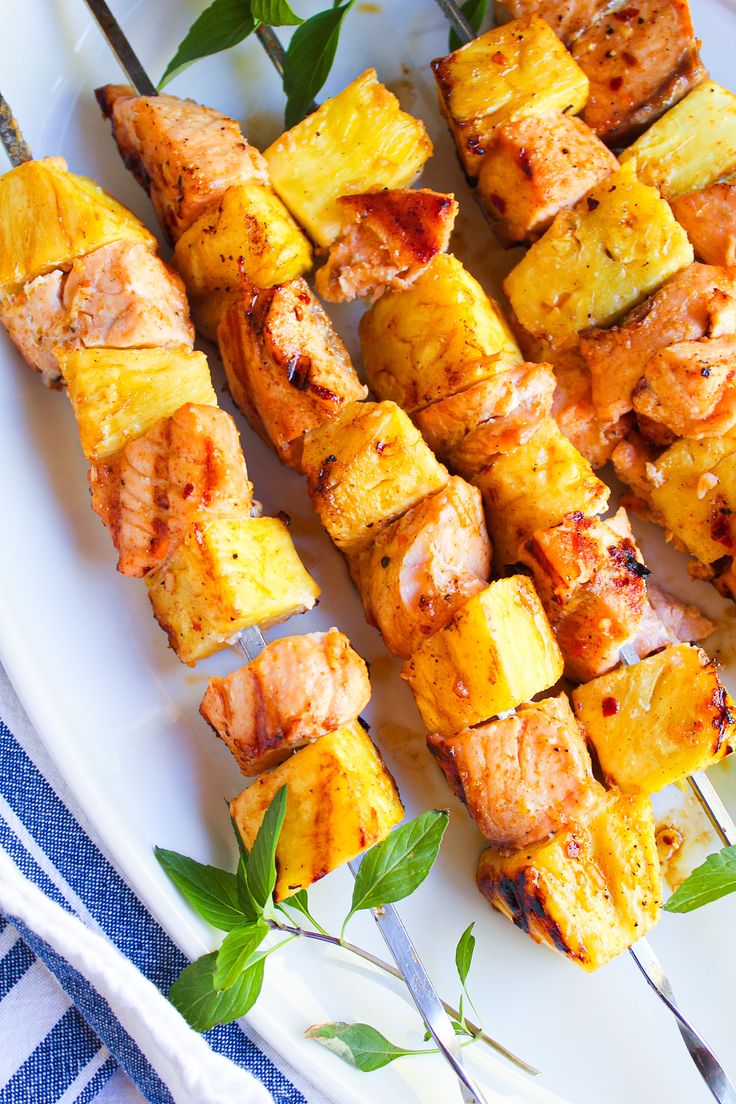 pineapple chicken kabobs on a white plate with silverware and green leaves