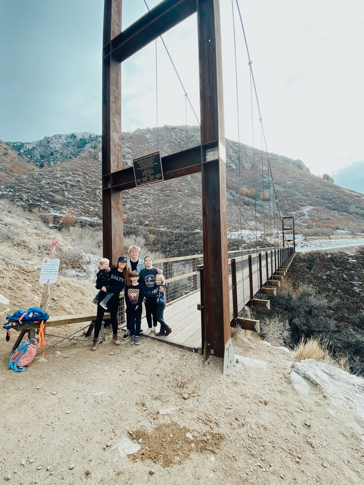 some people are standing on a bridge over water and sand with mountains in the background