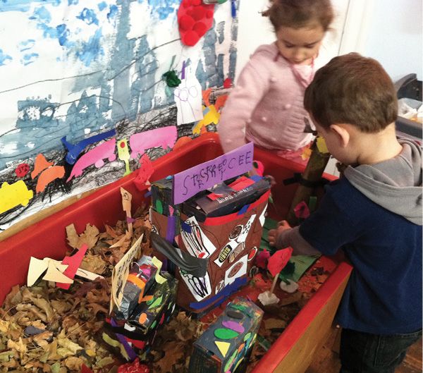 two young children playing with toys in a play room filled with leaves and other things