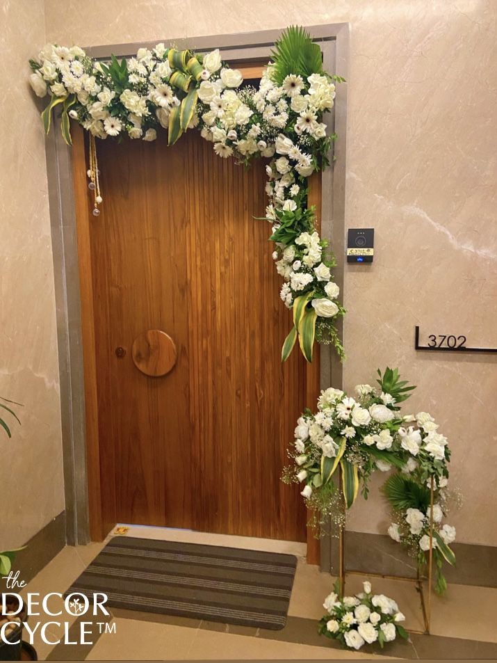 a door decorated with white flowers and greenery next to a mat on the floor