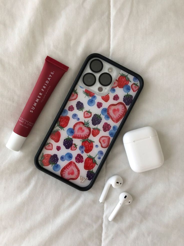 an iphone case with strawberries and berries on it next to earbud plugs