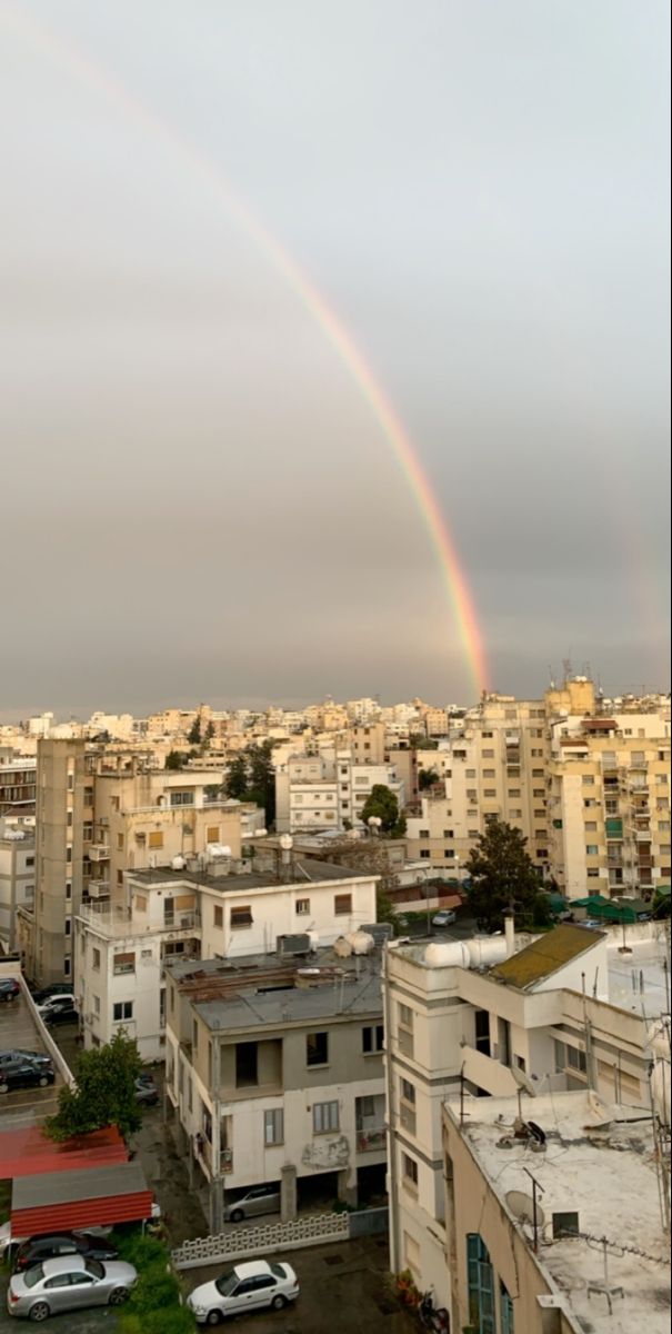 a rainbow in the sky over a cityscape with cars parked on the street