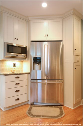 a stainless steel refrigerator in a kitchen with white cabinets and wood flooring on the side