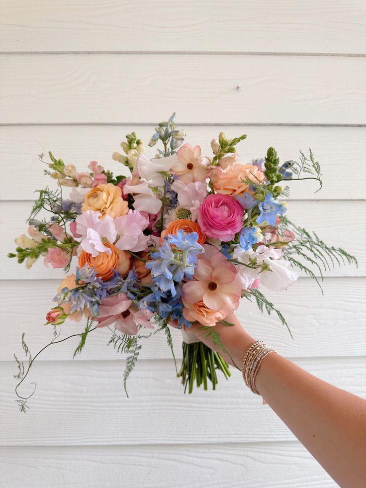 a person holding a bouquet of flowers in front of a white wall with wood planks