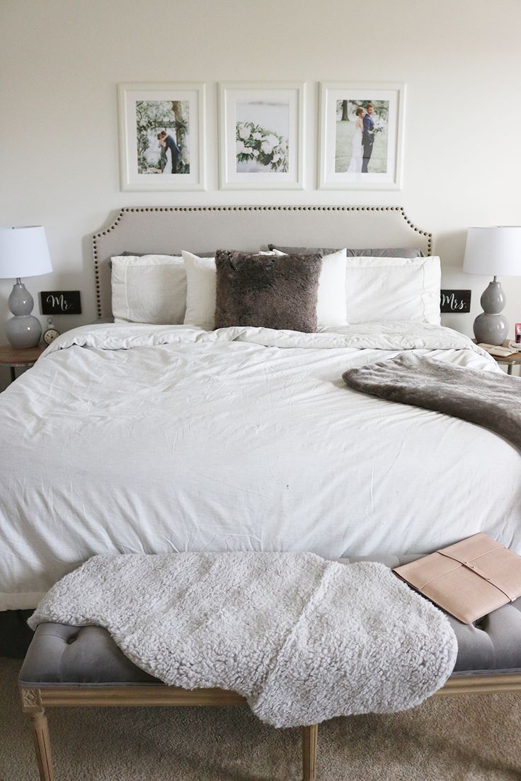 a bed with white comforter and pillows in a small room next to two pictures on the wall