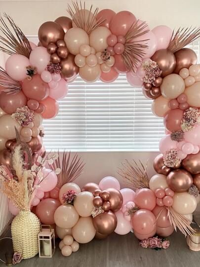 a pink and gold balloon arch with palm leaves, flowers and other decorations on it