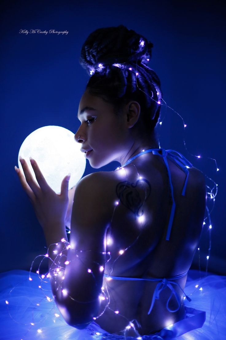 a woman holding a ball in her hand with blue lights around her and the moon behind her