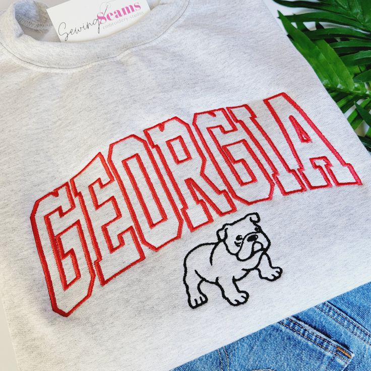 Experience the perfect blend of style and school spirit with our Georgia Bulldog Crewneck Sweatshirt or T-shirt! Available in three colors, this sweatshirt is designed to keep you cozy and comfortable, whether you're cheering in the stands or just showing off your Bulldog pride around town. At the heart of its design is the iconic "Georgia" embroidery, boldly presented across the center chest. The word is intricately stitched in a vibrant red, capturing the essence of the University of Georgia's Georgia Bulldogs Shirts Vinyl Men, Crew Neck Hoodie With Embroidered Logo For College, Collegiate Sweatshirt With Embroidered Graphics, Varsity Sweatshirt With Letter Embroidery For Campus, Varsity Letter Embroidery Sweatshirt For Campus, Varsity Sweatshirt With Letter Embroidery For College, Varsity Style Sweatshirt With Letter Embroidery For Campus, Varsity Style Letter Embroidery Sweatshirt For Campus, College Fan Apparel Hoodie With Embroidered Logo