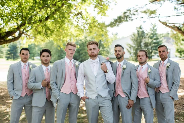 a group of men standing next to each other in front of a tree and grass field