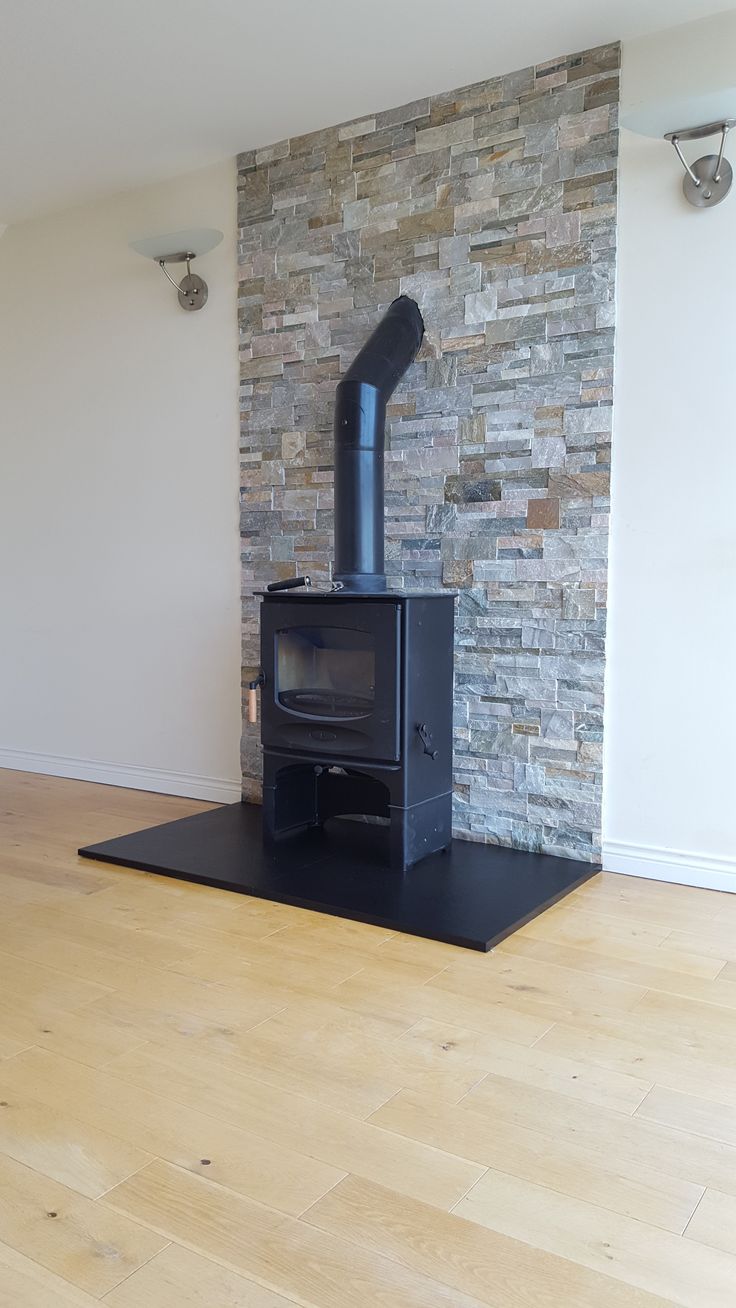 a black stove sitting on top of a wooden floor next to a stone wall in an empty room