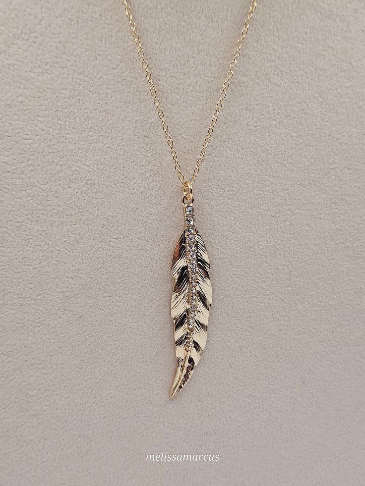 18-inch gold necklace with gold feather pendant that is approximately 2 inches in length and 1 cm wide with rhinestones going down the center of the pendant. Feather Necklace Gift, Elegant Feather Dangle Jewelry, Elegant Feather Jewelry As Gift, Elegant Feather Jewelry Gift, Elegant Feather Jewelry For Gift, Gold Feather Necklace Perfect For Gifting, Gold Feather Necklace For Gift, Gold Necklace With Feathers As A Gift, Gold Necklace With Feathers For Gift