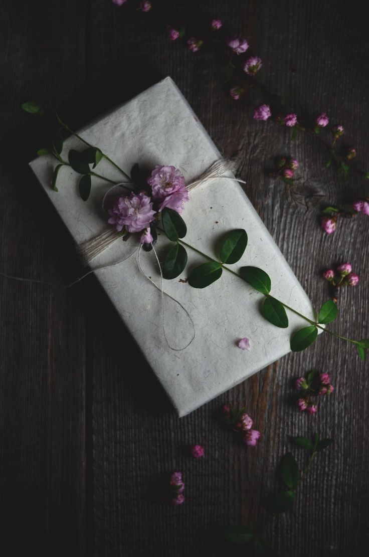 a gift wrapped in white paper with pink flowers on the top and green leaves around it