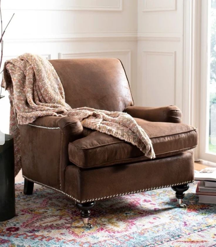 a brown chair with a blanket on it in front of a window next to a vase