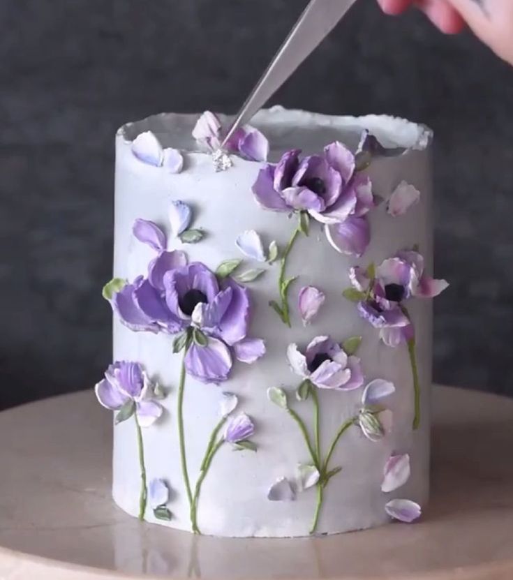 a person cutting into a cake with purple flowers on the frosting and white icing