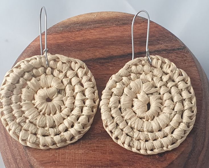 pair of woven earrings on wooden surface with white background and wood disc shape ear wires