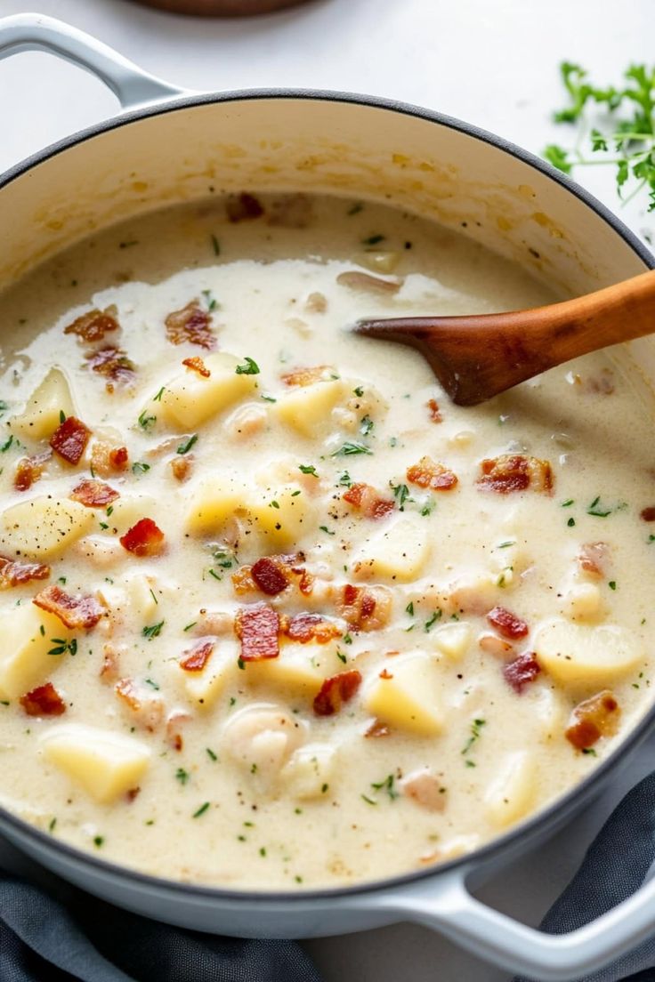 a pot filled with potatoes and bacon on top of a white countertop next to a wooden spoon