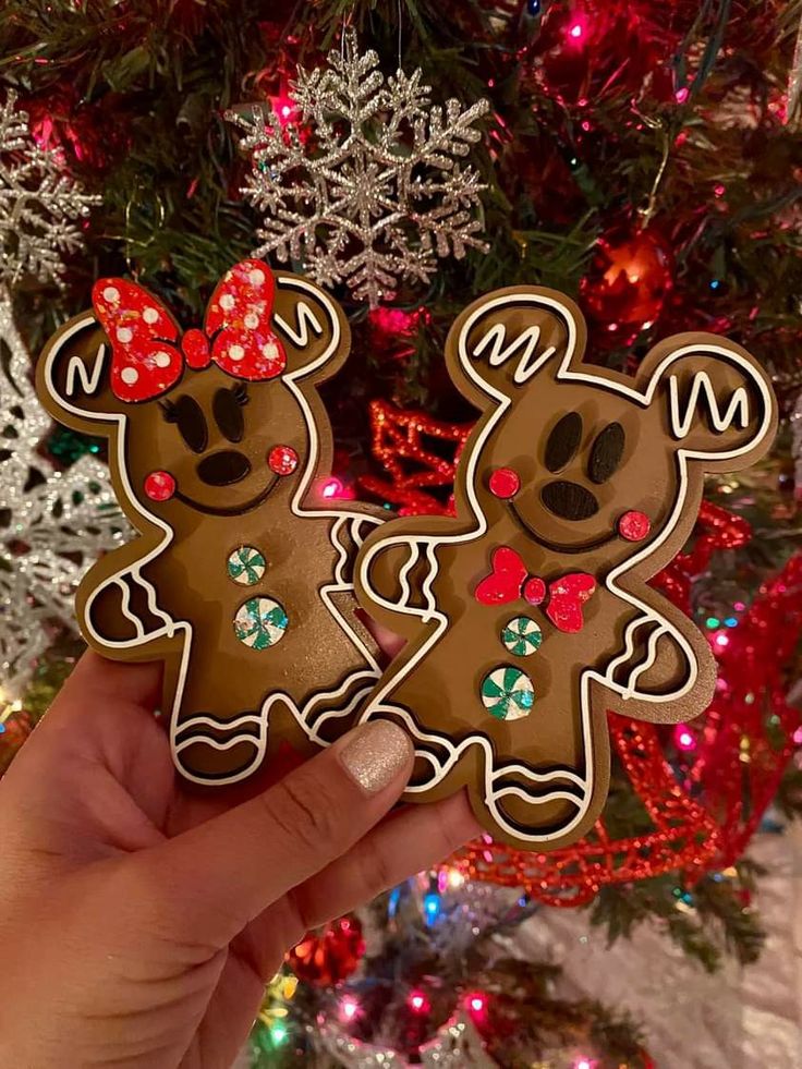 someone holding up two decorated cookies in front of a christmas tree