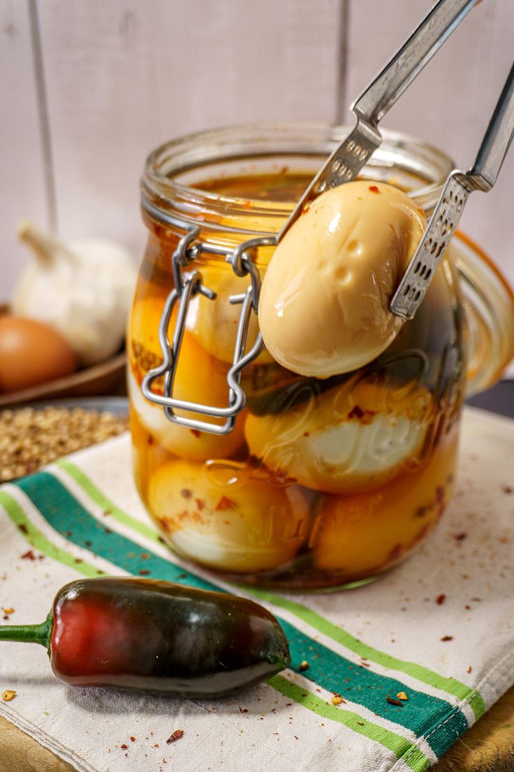 a jar filled with pickles and sauce on top of a towel next to an eggplant